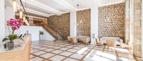 A spacious lobby with a checkered floor, a reception desk, a staircase, and stone walls.