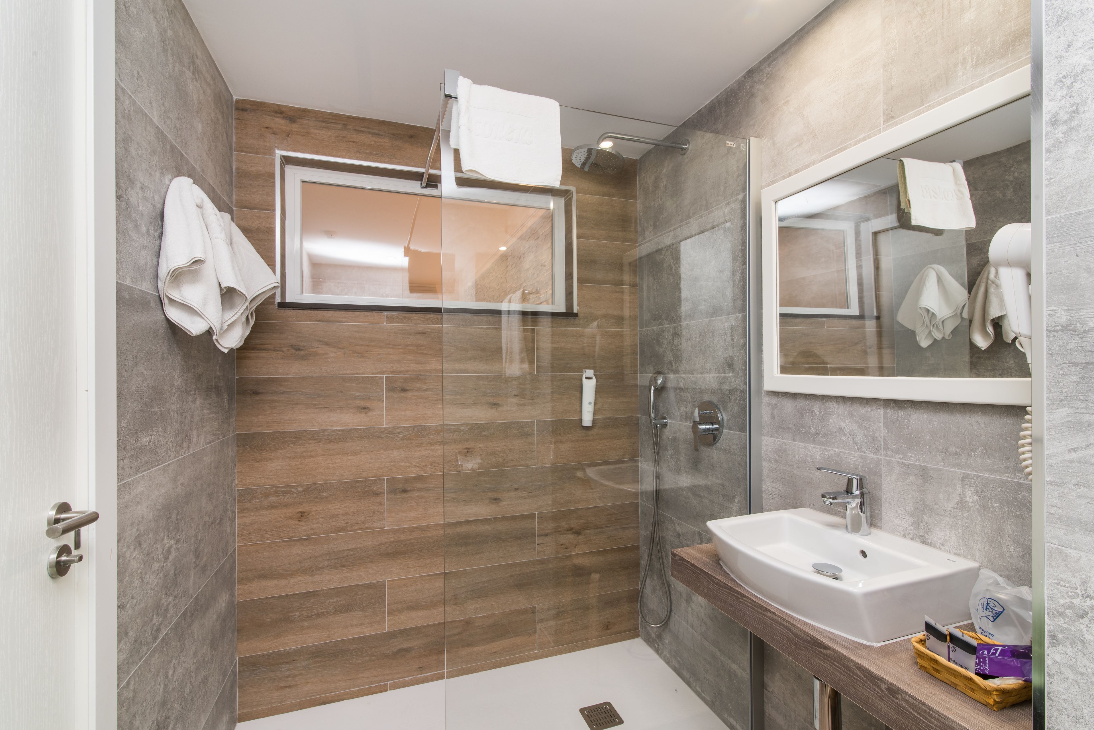 Un baño moderno con cabina de ducha de vidrio, pared de madera, espejo grande y lavamanos blanco.