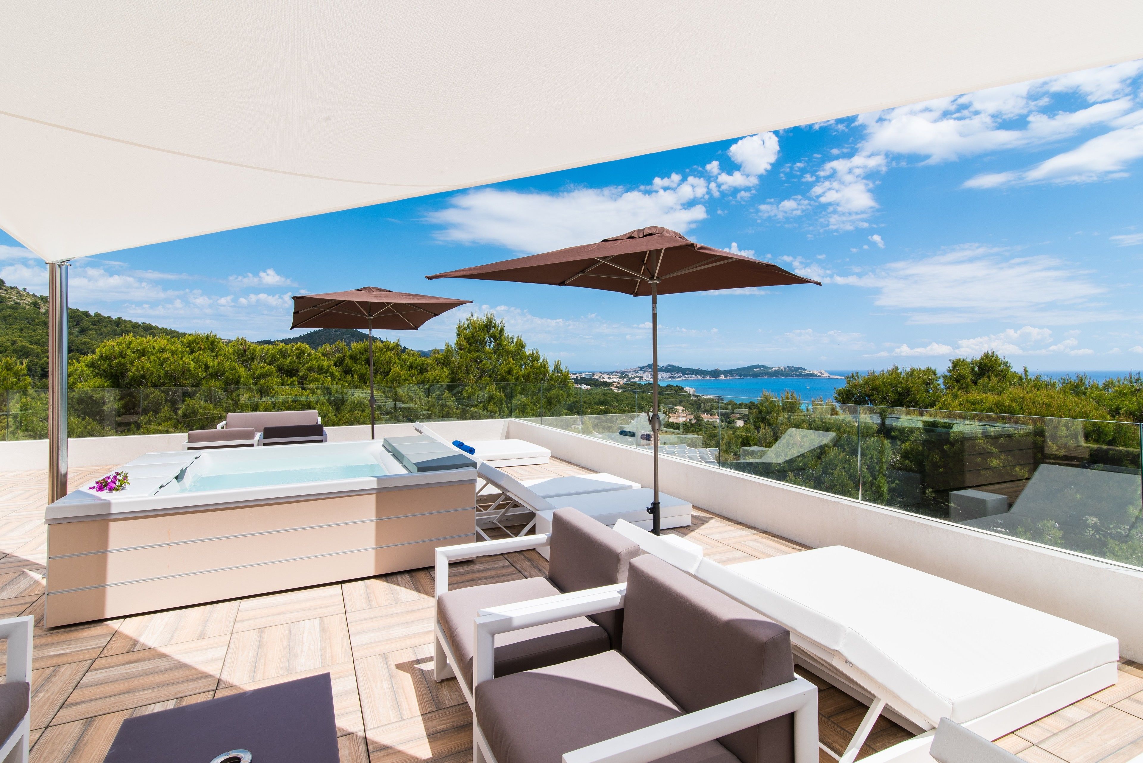 A rooftop terrace with a hot tub, lounge chairs, and umbrellas, overlooking a scenic landscape.