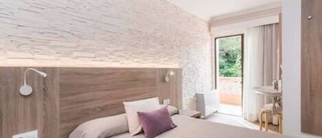 A modern bedroom with a stone wall, a wooden headboard, a bed with a white and purple pillow, a bedside table with a lamp, and a view of the outdoors.