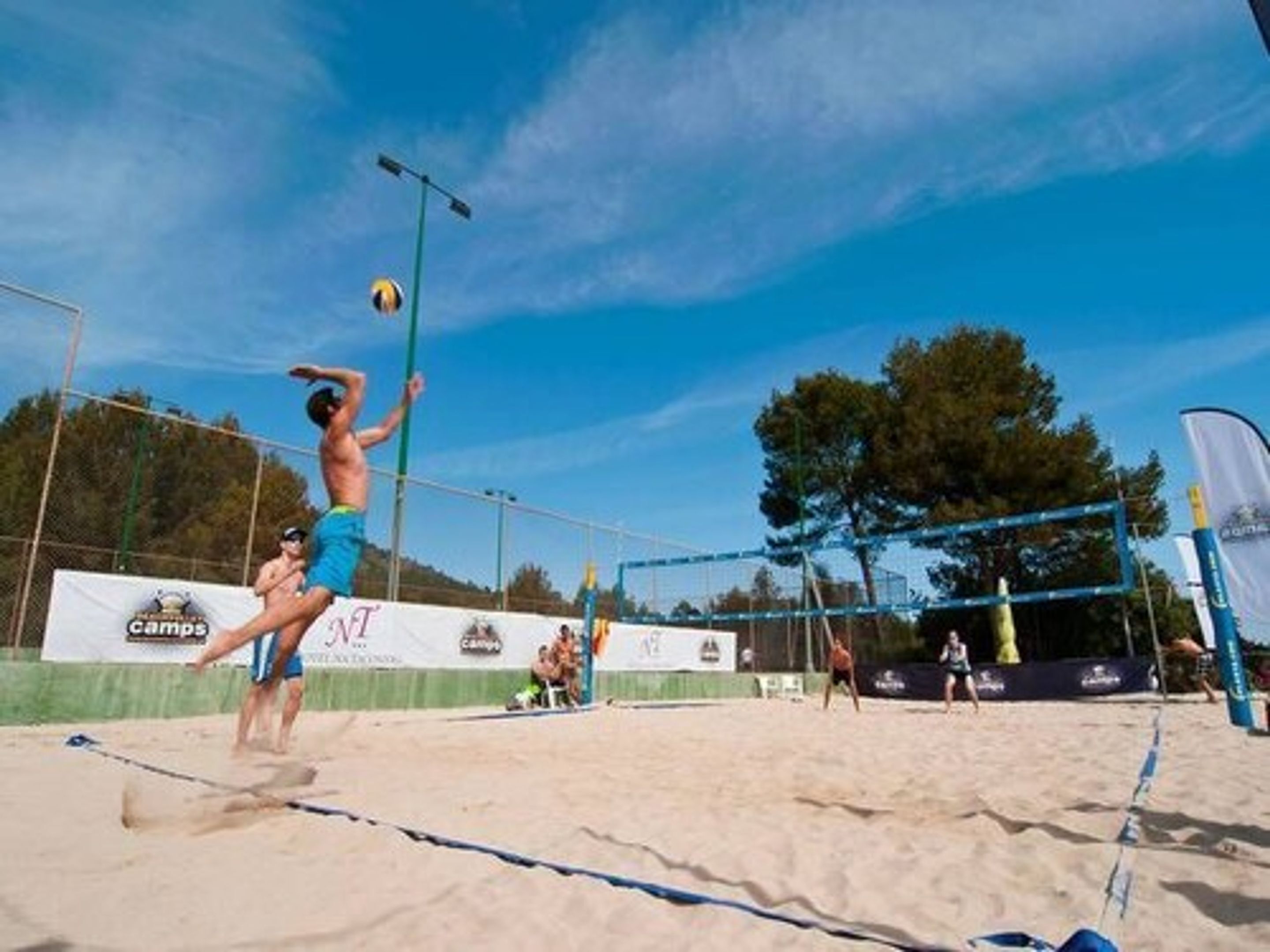 A beach volleyball game with players in blue shorts and a net in the center.