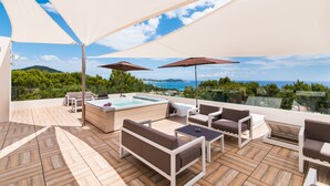 Una terraza en la azotea con jacuzzi, mobiliario exterior y una vista panorámica del mar y las colinas.
