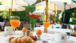 An outdoor dining area with tables, umbrellas, and a breakfast setting including croissants, eggs, and orange juice. - Cala Gat (Capdepera)