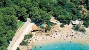 An aerial view of a coastal area with a beach, rocky outcrops, and dense greenery. - Cala Gat (Capdepera)