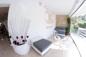 A modern interior with a white reception desk, a sofa, and a potted plant. - Cala Gat (Capdepera)