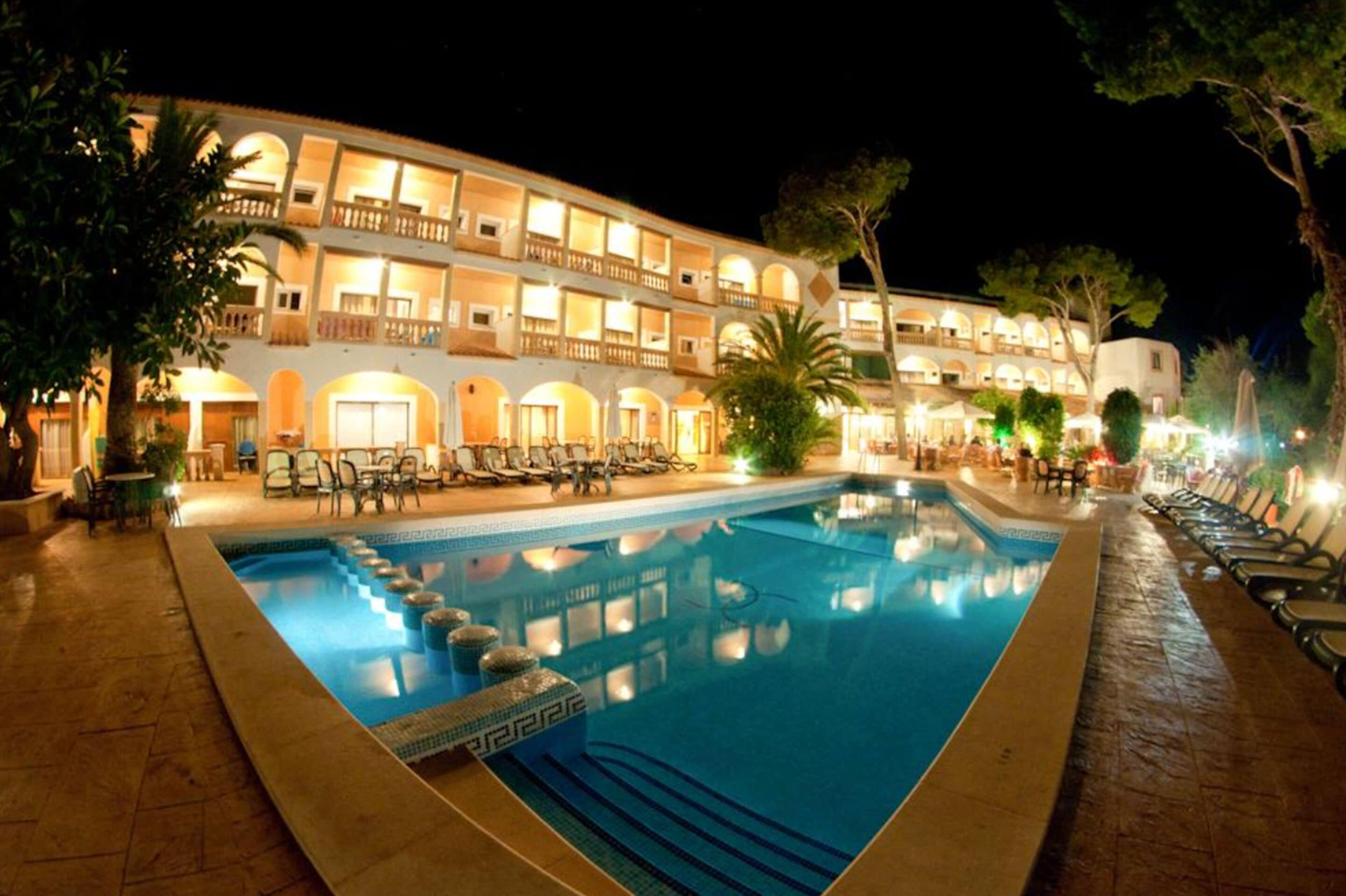 A hotel with a swimming pool, outdoor seating, and a well-lit facade.