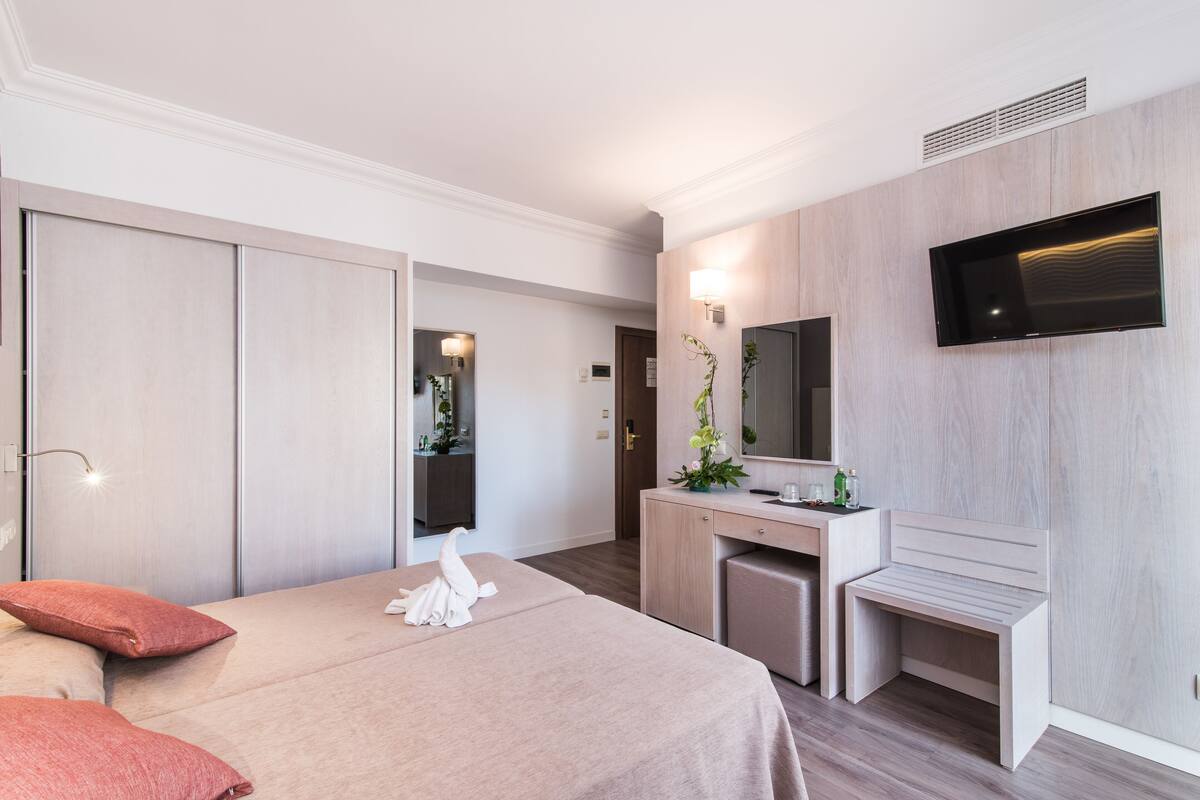 A hotel room with a bed, a desk, a mirror, and a TV.