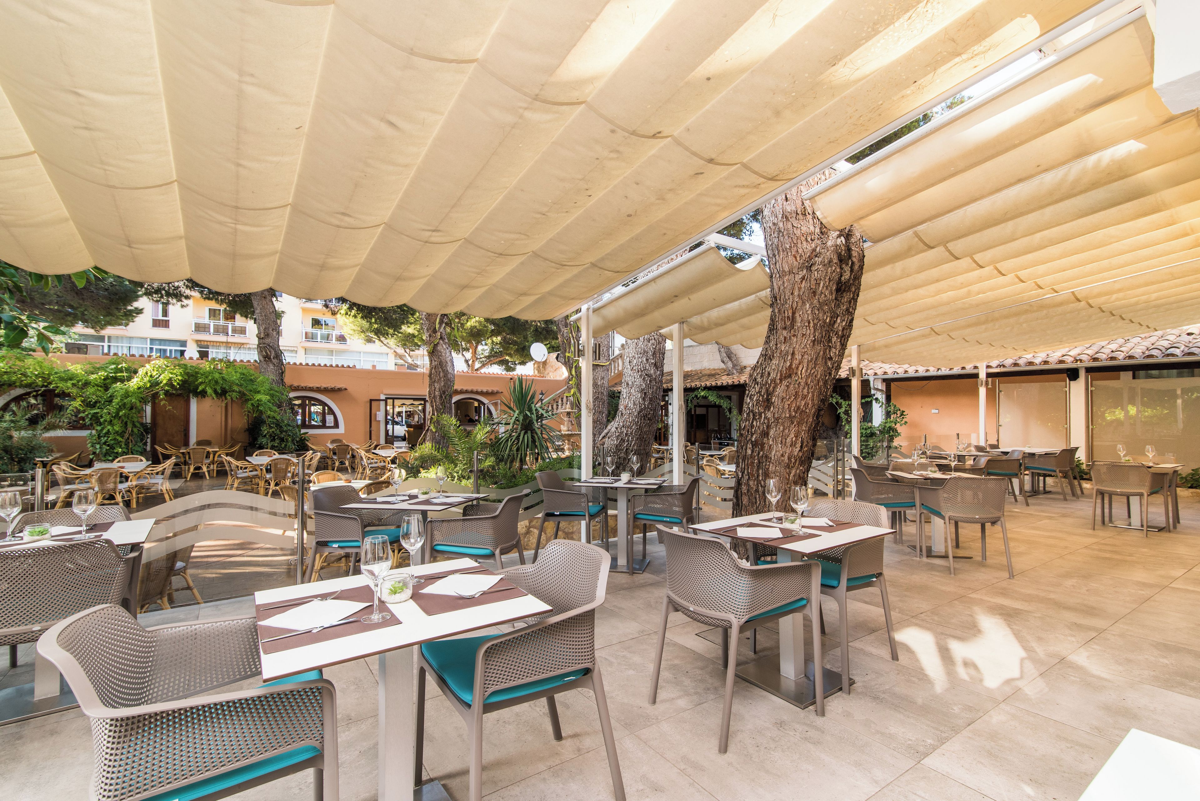 An outdoor cafe with tables and chairs, surrounded by trees and buildings.