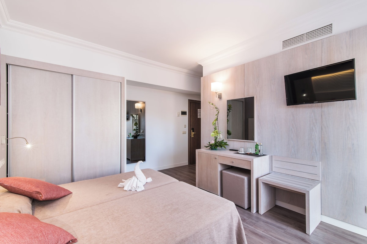 A hotel room with a bed, a desk, a mirror, and a TV.