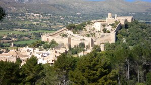 A historic castle with a fortified wall, situated on a hill overlooking a coastal town. - Baviera Hotel (Capdepera)