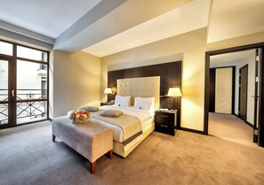 Een hotelkamer met een groot bed, nachtkastjes, een bankje en uitzicht op het omliggende landschap.