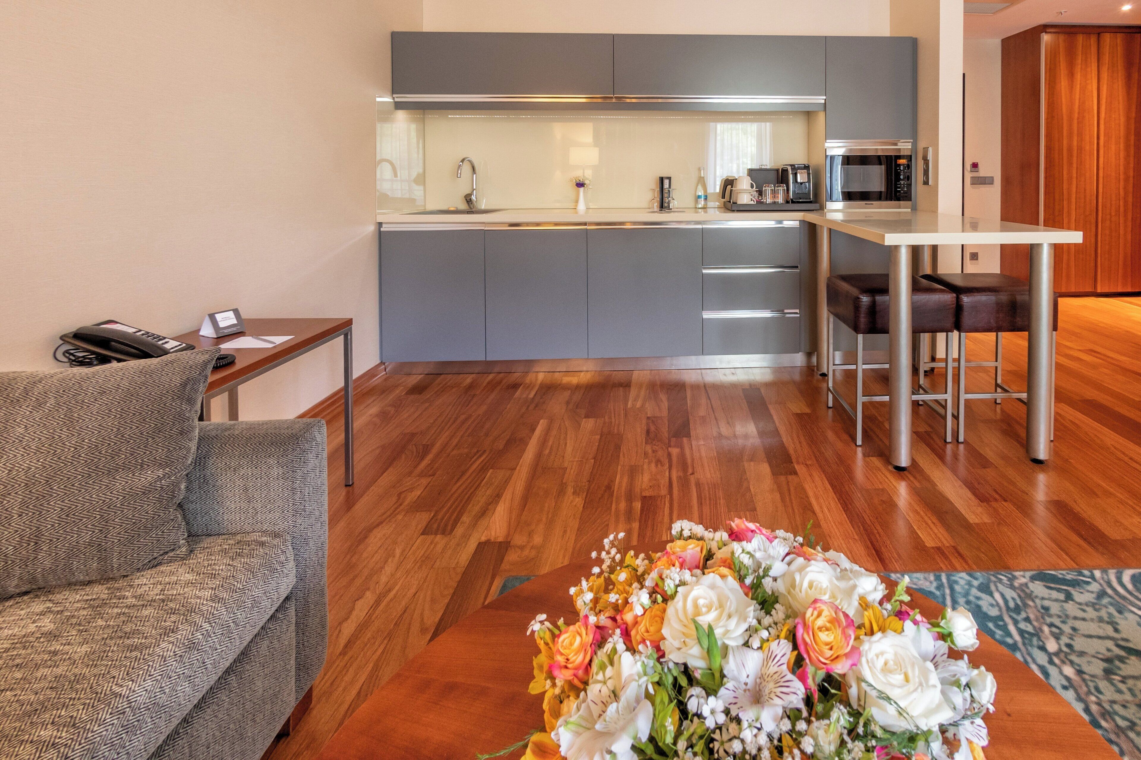 A modern living room with a sofa, a coffee table with flowers, a kitchen area with a microwave, and a dining table.