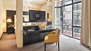 Een moderne hotelkamer met een donker houten bureau, een flatscreen televisie, een gele stoel en een balkon met buitenmeubilair.