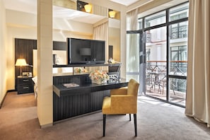 Une chambre d’hôtel moderne avec un bureau en bois foncé, un téléviseur à écran plat, une chaise jaune et un balcon aménagé avec du mobilier d’extérieur.