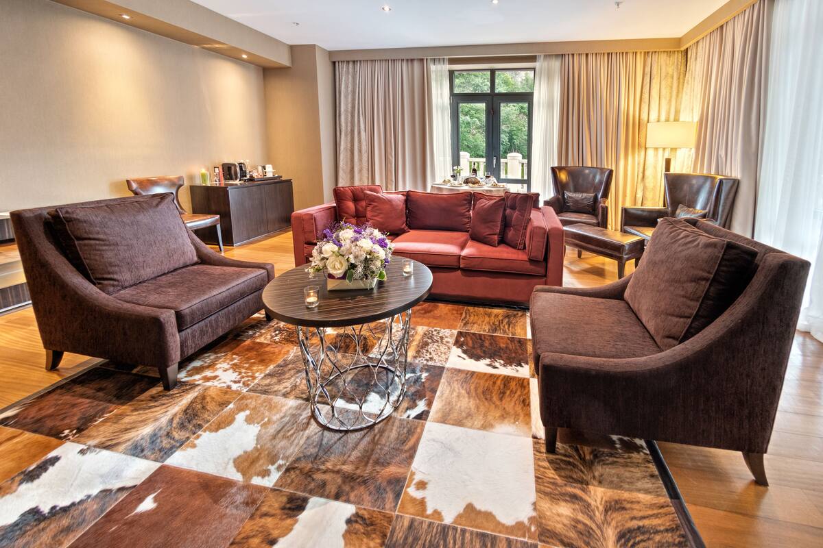 Una sala de estar moderna con un sofá rojo, dos sillones, una mesa de centro y una zona de bar con una lámpara.