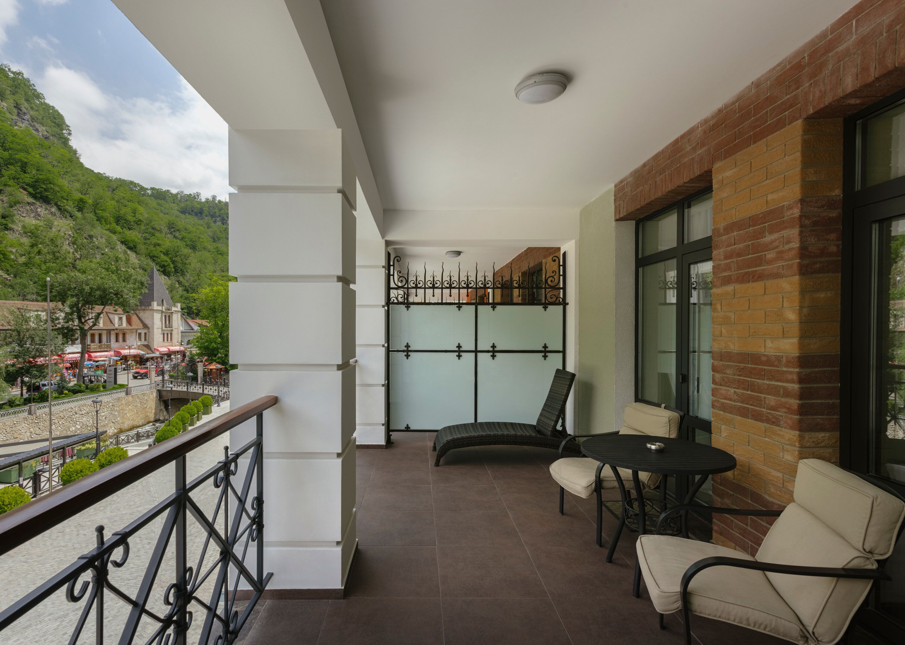 A balcony with a view of a town, a brick wall, and a table with chairs.