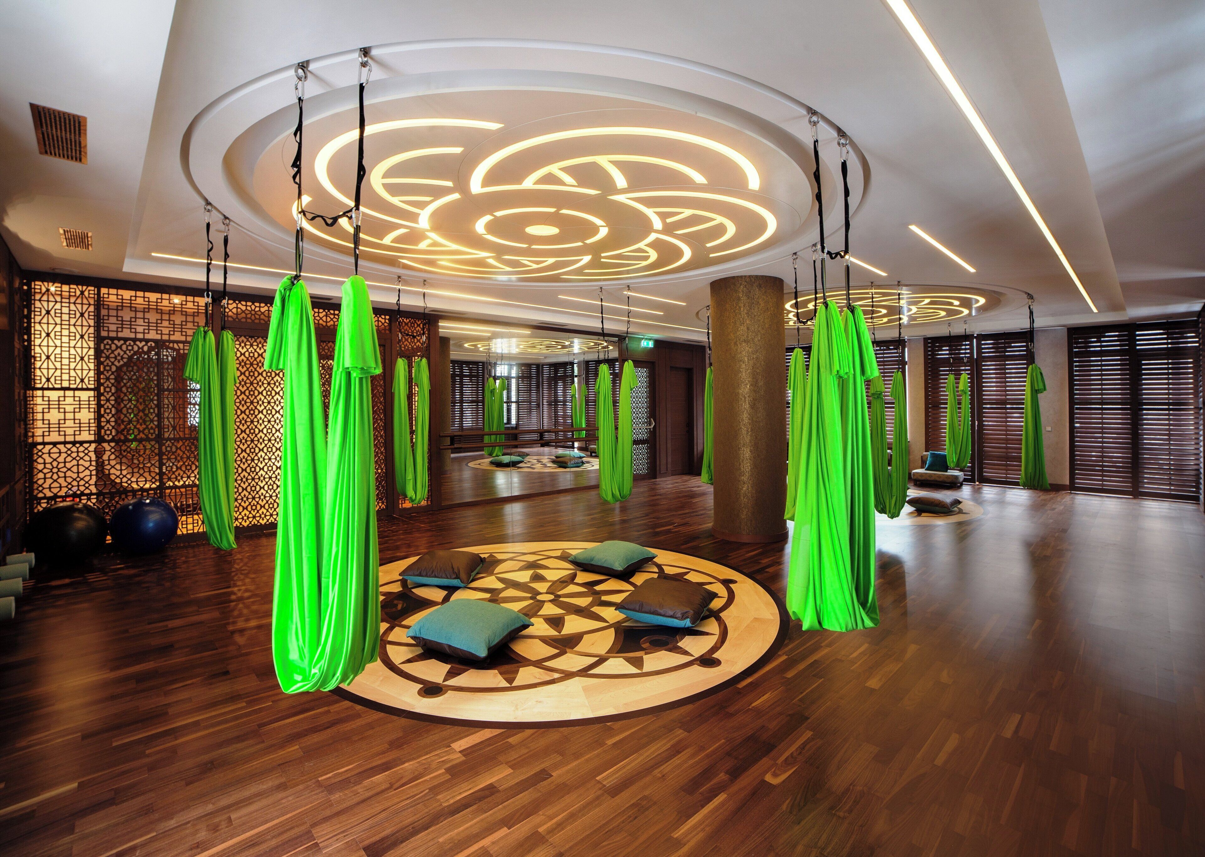 A spacious room with a wooden floor, green hanging fabric structures, and a circular patterned rug.