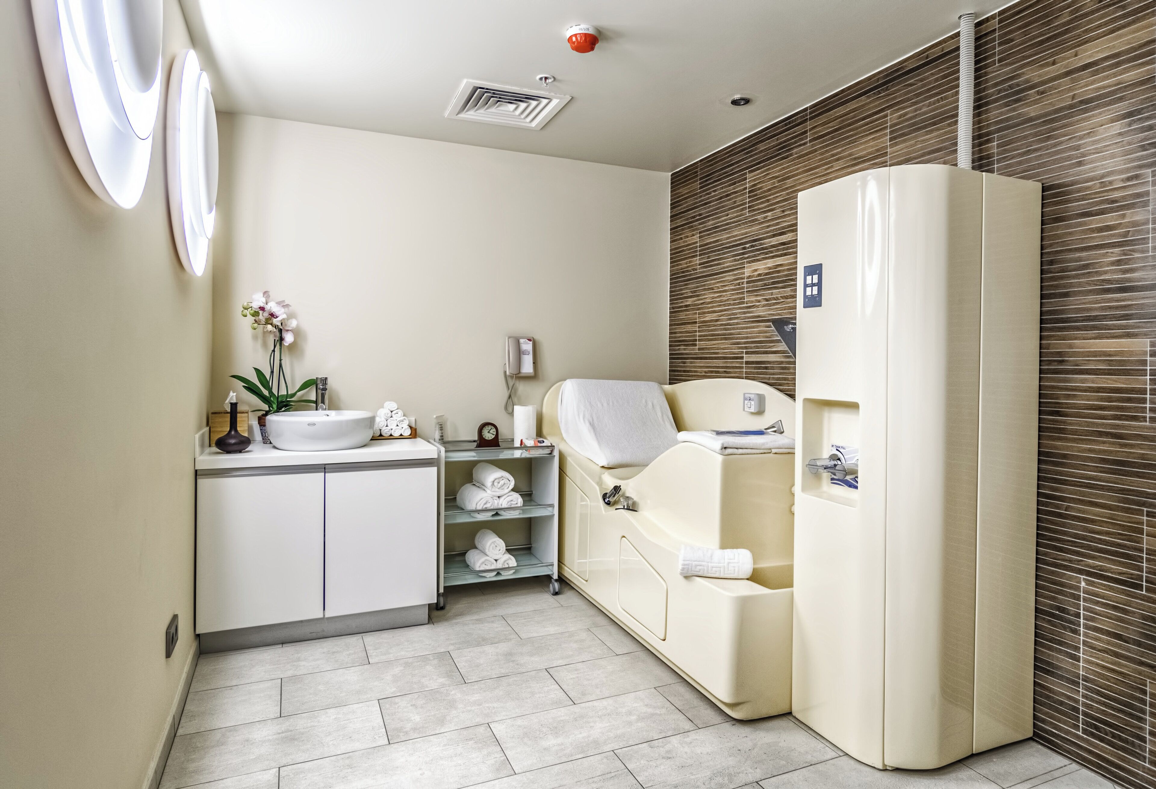 A modern bathroom with a sink, mirror, towel rack, and a massage chair.