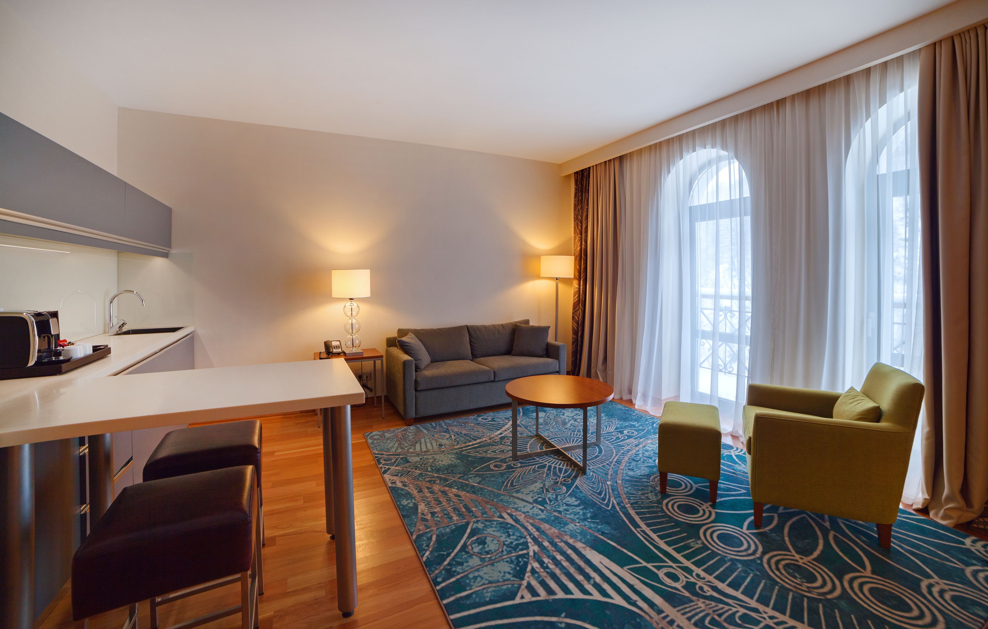 A hotel room with a dining area, a sofa, a yellow armchair, and a patterned rug.