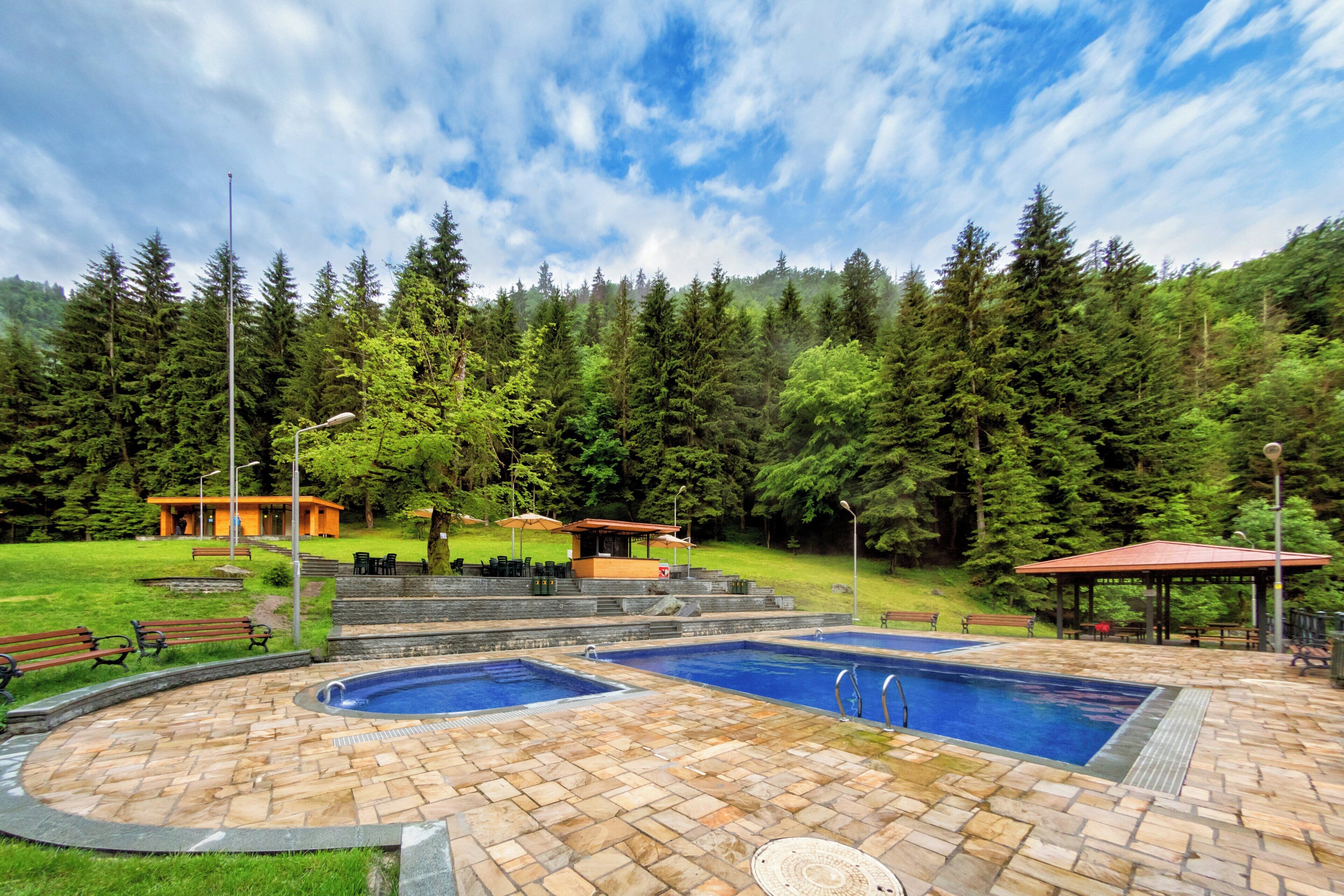 Un área de piscina con dos piscinas, una zona de estar techada y un edificio al fondo.