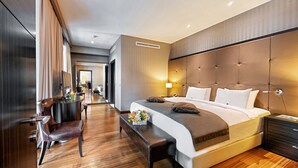 Quarto de hotel moderno com uma cama grande, um banco de madeira, uma escrivaninha com uma cadeira e vista para o corredor.