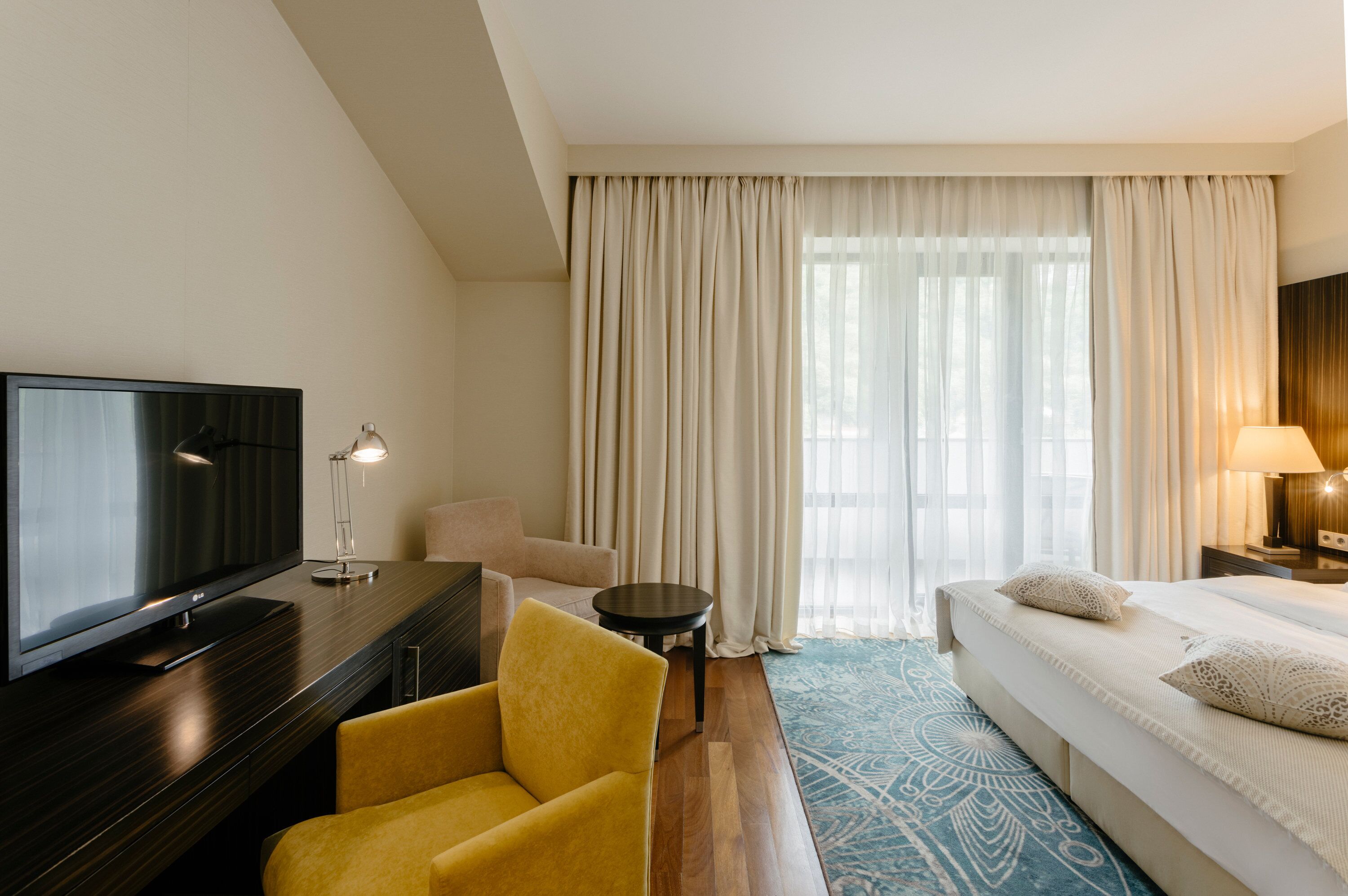 Une chambre d’hôtel avec un lit, une télévision, un fauteuil jaune, une petite table et une lampe.