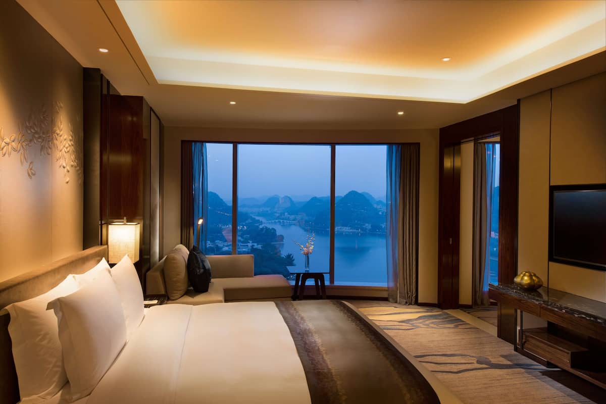 Habitación de hotel con una cama grande, televisor, escritorio y vistas a una masa de agua.