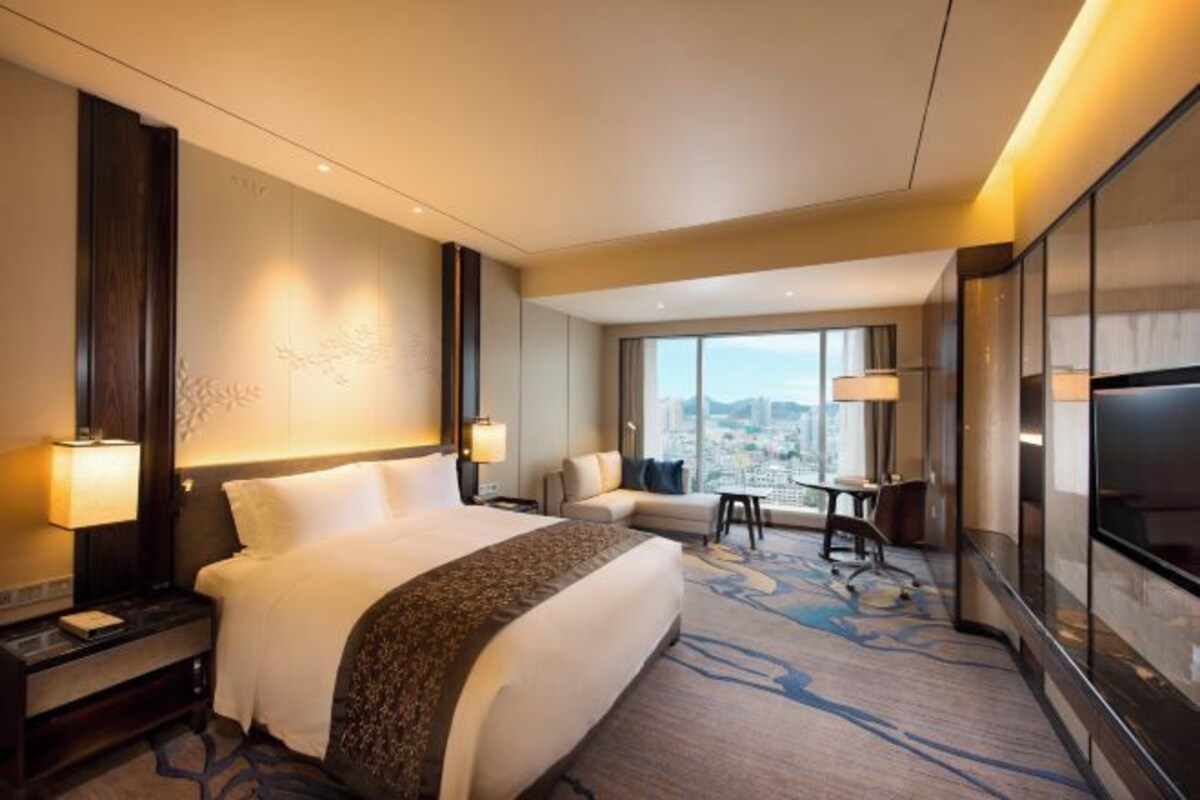 A hotel room with a large bed, a desk, a chair, and a TV.