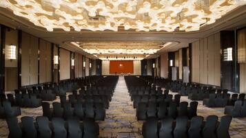 A conference room with rows of chairs, a large screen at the front, and a modern chandelier.