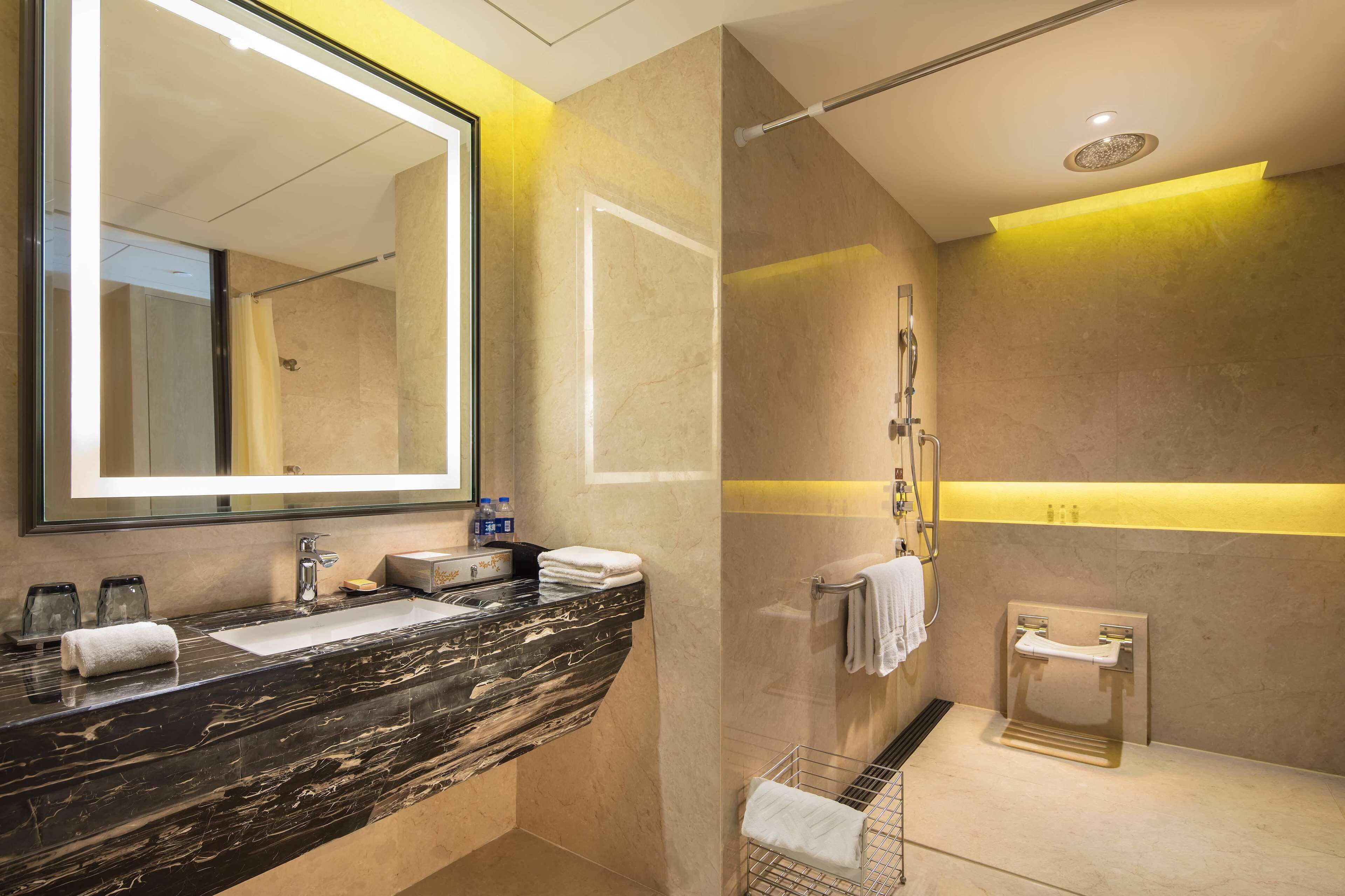 A modern bathroom with a marble vanity, a large mirror, and a glass shower enclosure.