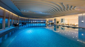 An indoor swimming pool with a modern ceiling design, lounge chairs, and a view of the cityscape. - DoubleTree by Hilton Hotel Anshun (Anshun)