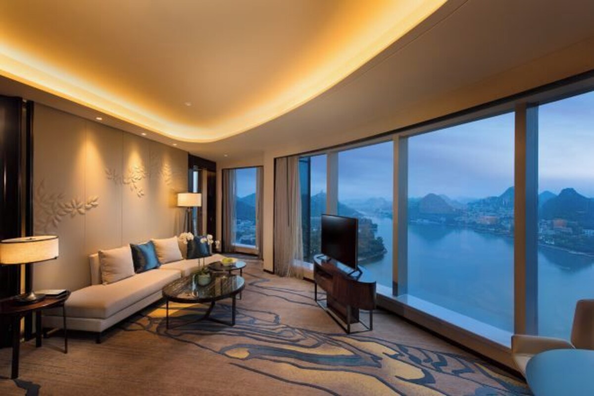 A modern hotel room with a large window offering a view of a body of water and mountains.