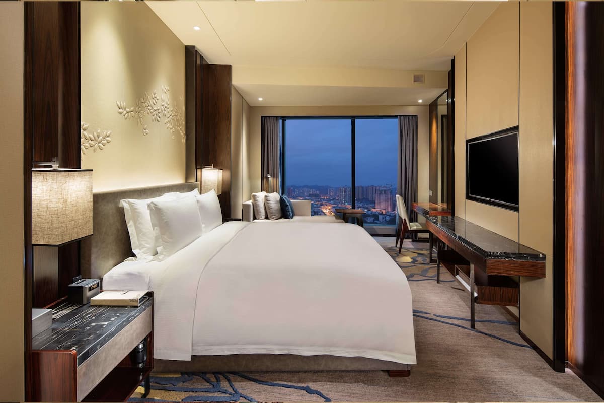 Habitación de hotel con una cama grande, un escritorio con televisión de pantalla plana, vistas a la ciudad y un diseño moderno.