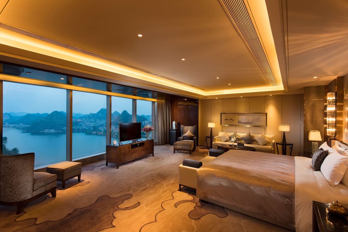 Una habitación de hotel moderna con una cama grande, televisión, escritorio y vistas a un lago y montañas.