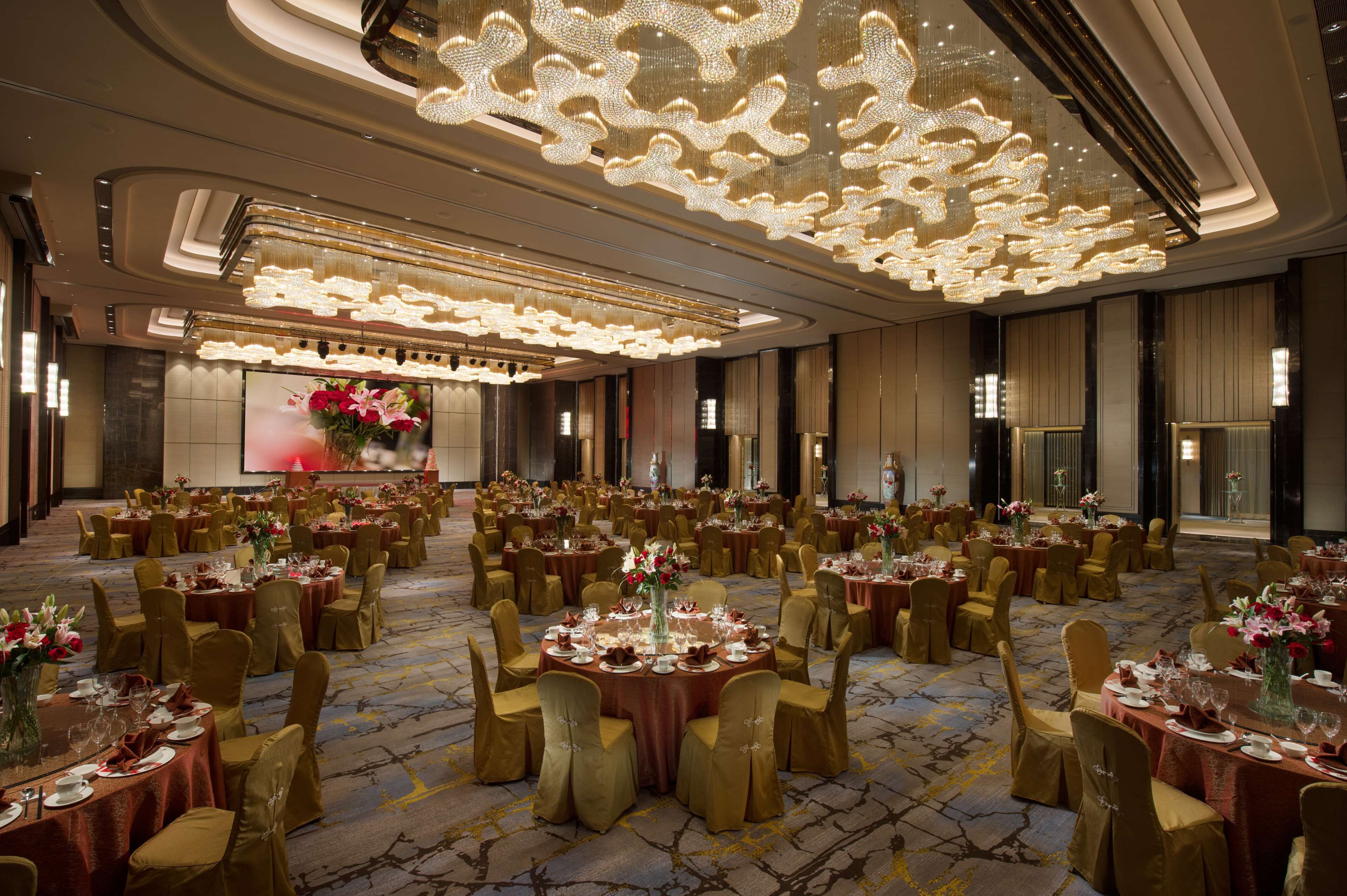 A large banquet hall with round tables, gold chairs, and chandeliers.