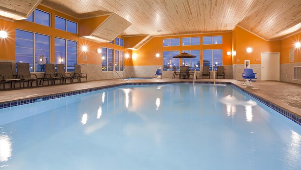 An indoor swimming pool with clear blue water, surrounded by wooden walls and large windows.