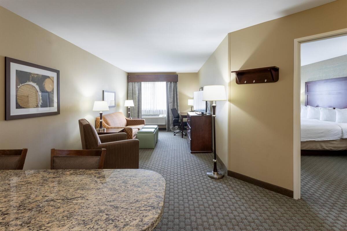 A hotel room with a dining table, chairs, a sofa, a desk, and a bed.