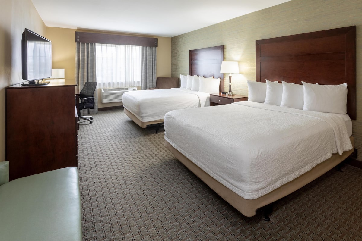 A hotel room with two beds, a desk, a chair, a TV, and a window with curtains.