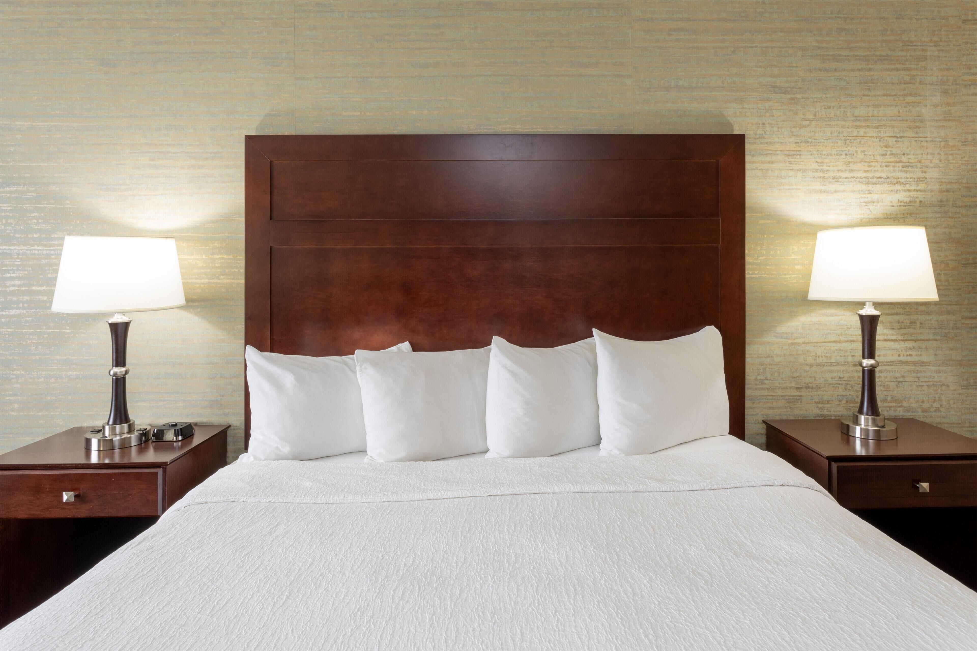 Une chambre d’hôtel avec un grand lit, deux tables de chevet et des lampes.