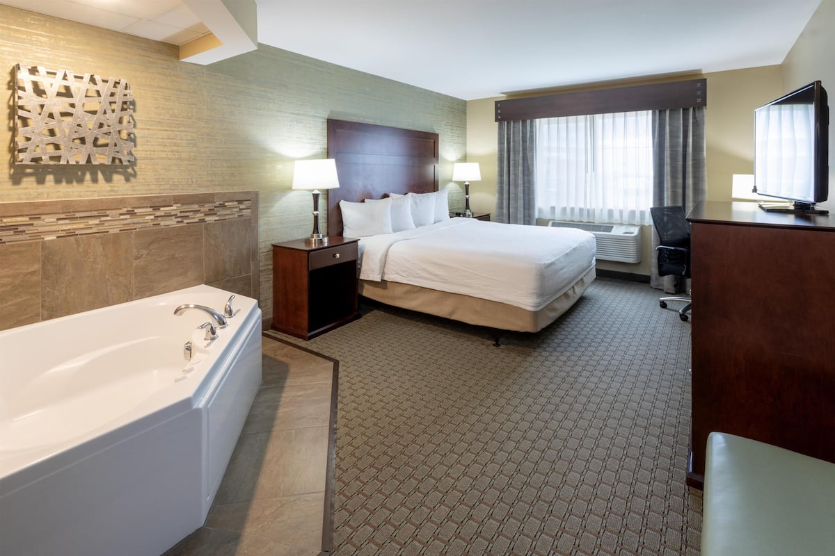 A hotel room with a large bed, a separate bathroom with a bathtub, a desk with a chair, and a television.