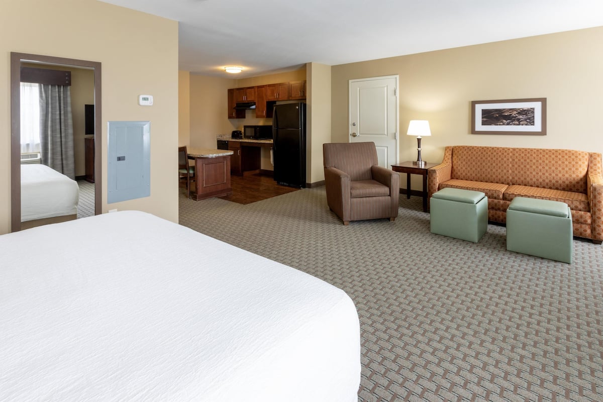 A hotel room with a large bed, a sofa, a chair, a small table, and a kitchenette.