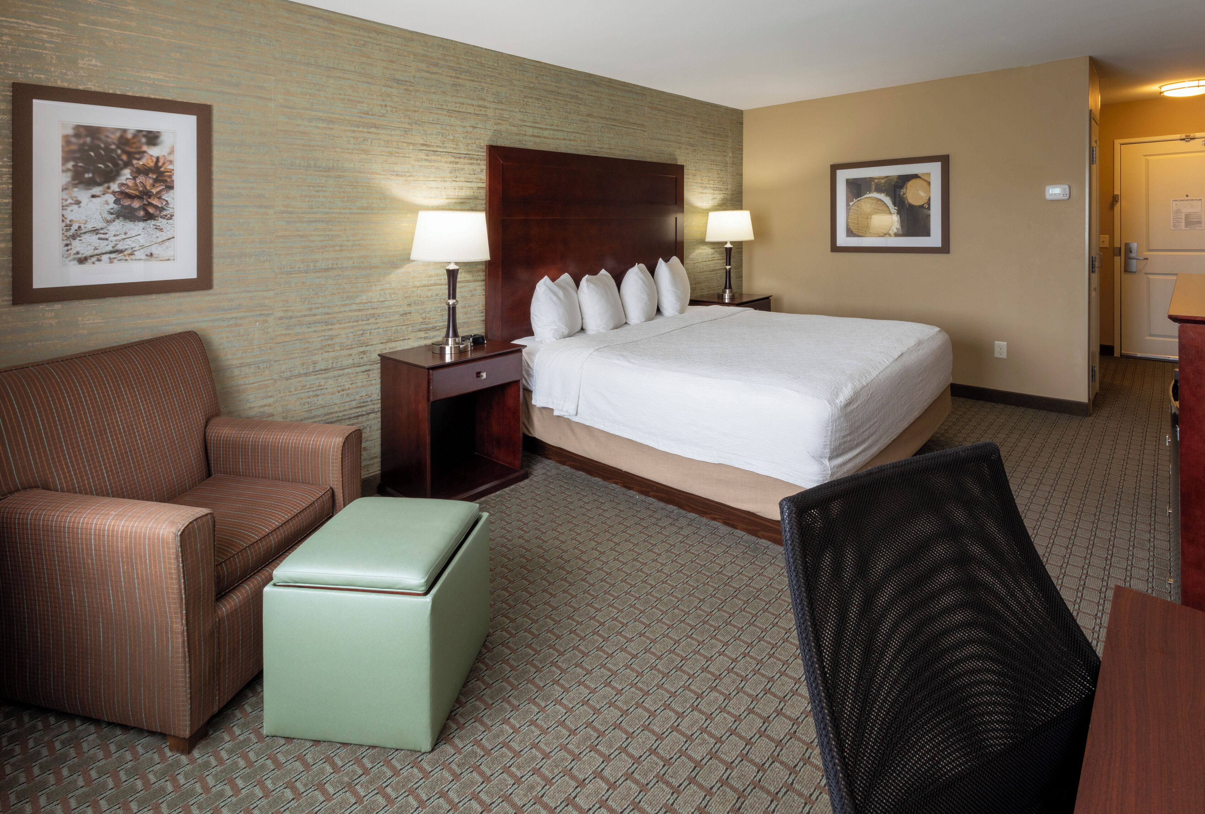 Une chambre d’hôtel comprenant un lit, deux tables de chevet avec des lampes, une chaise, une petite table et un tableau accroché au mur.