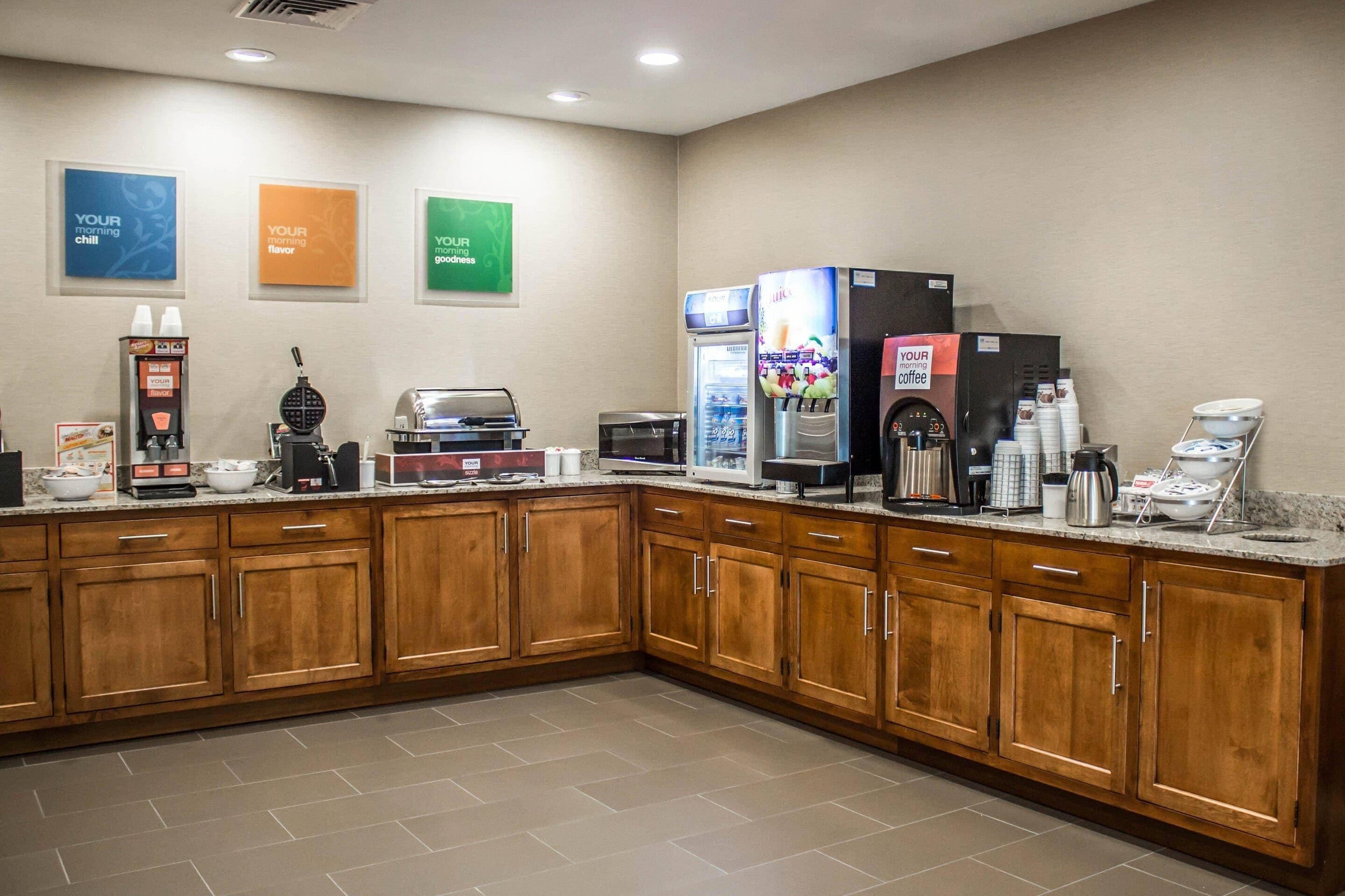 Uma cozinha de hotel com armários de madeira, máquina de café, micro-ondas e geladeira.