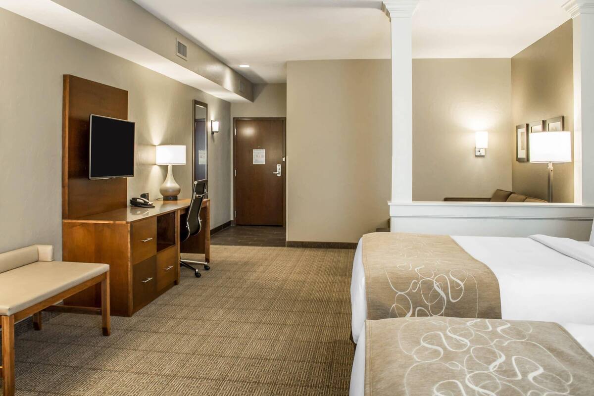 Een hotelkamer met een bed, bureau, stoel, televisie en een spiegel.