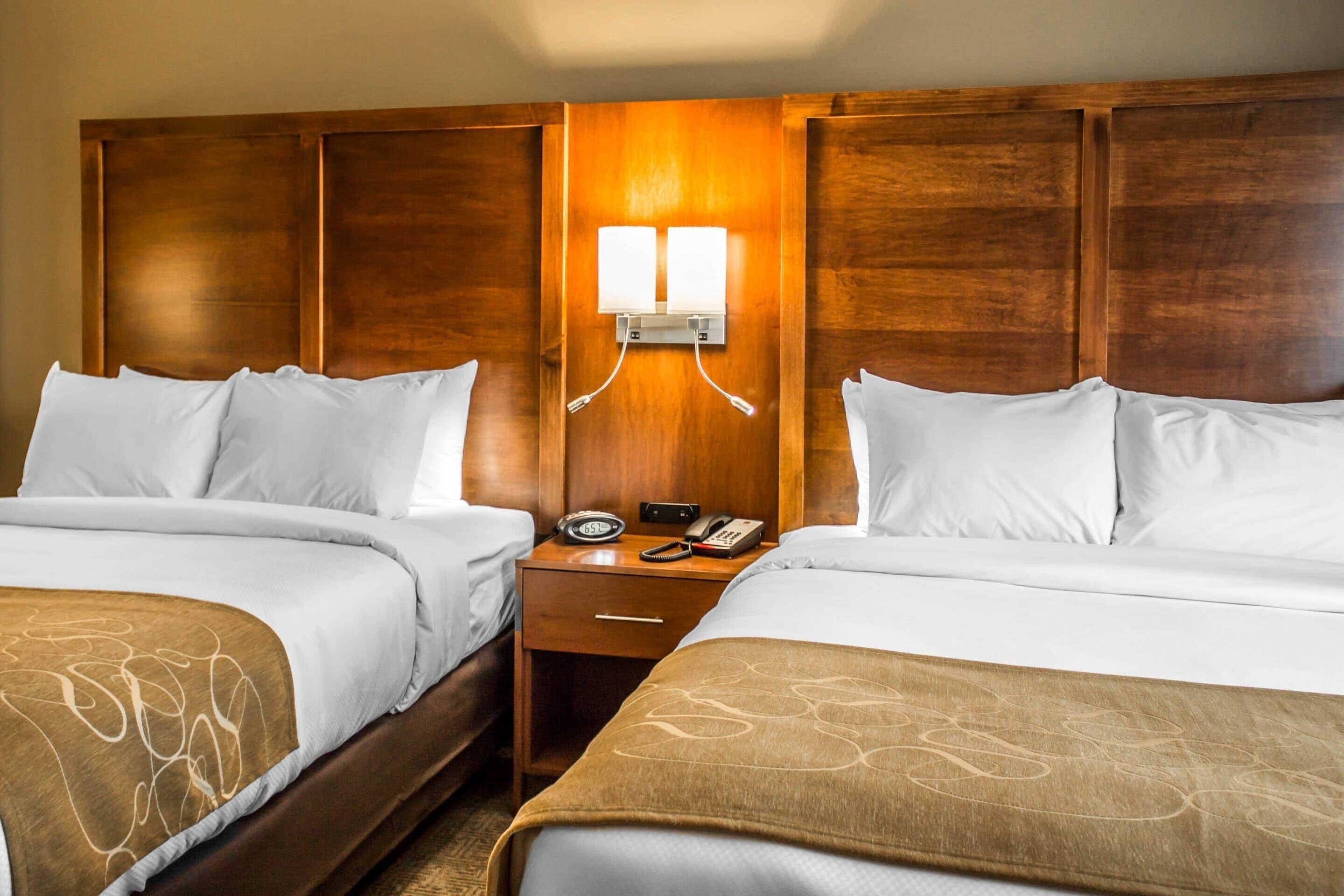 Habitación de hotel con dos camas, cabecera de madera, mesita de noche con un teléfono y una lámpara, y un aplique de pared.