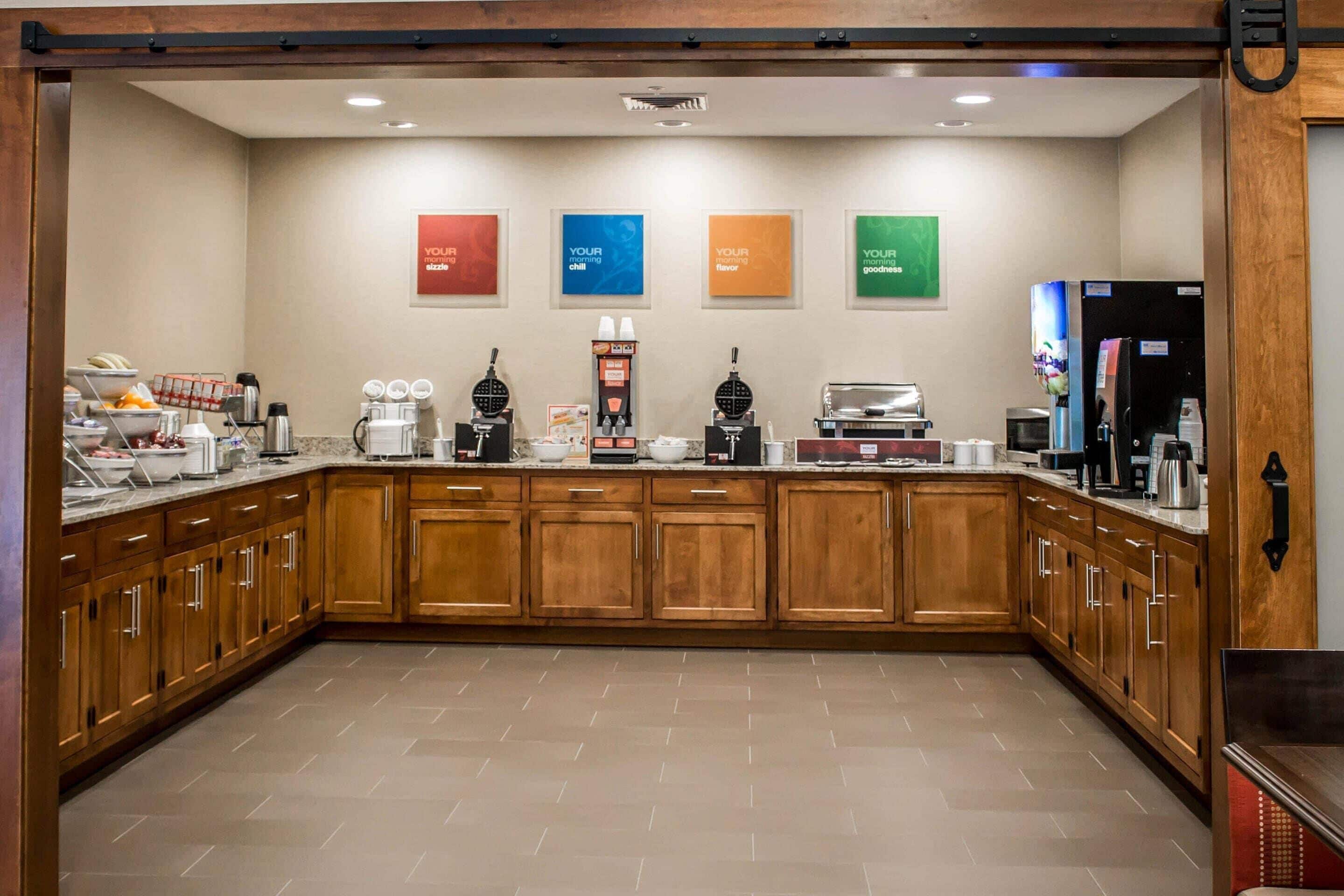 A hotel kitchen with wooden cabinets, a coffee station, and a refrigerator.