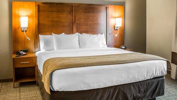 A hotel room with a large bed, wooden headboard, bedside lamps, a telephone, and a carpeted floor.