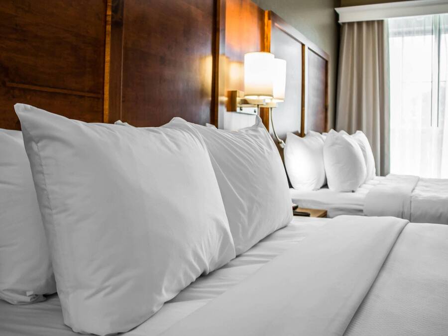Habitació d'hotel amb un llit gran, una tauleta de nit, una làmpada i una finestra amb cortines.