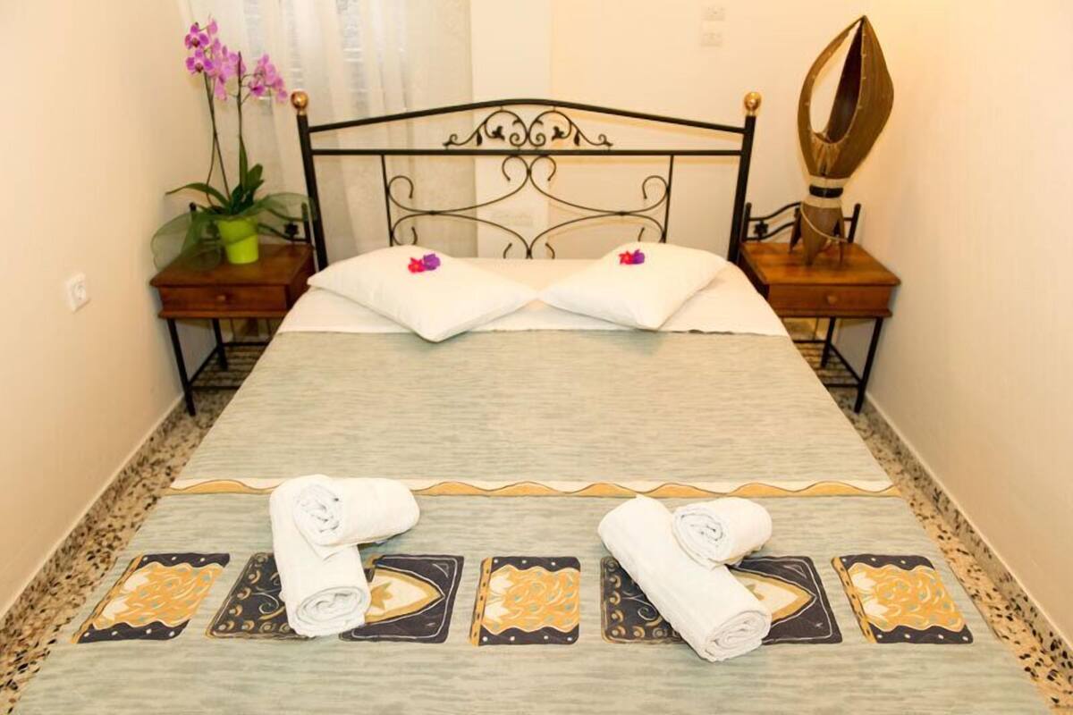 A neatly made bed with white linens, two pillows with pink flowers, and rolled towels on the floor.