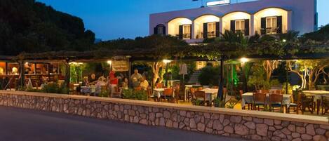 A restaurant with outdoor seating, a stone wall, and a building with flags in the background.